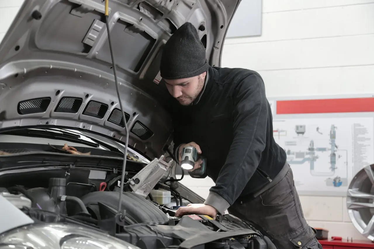 Mechanic inspecting car engine with flashlight in garage workshop