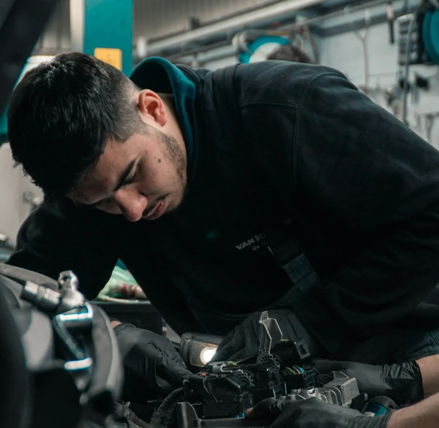 Mechanic working on car engine in workshop, using flashlight for detailed inspection