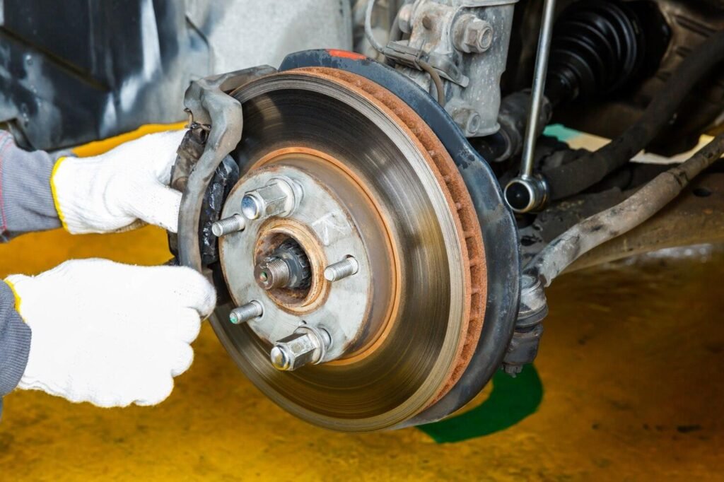 Mechanic wearing gloves repairing a car disc brake system with visible rotor and caliper parts.