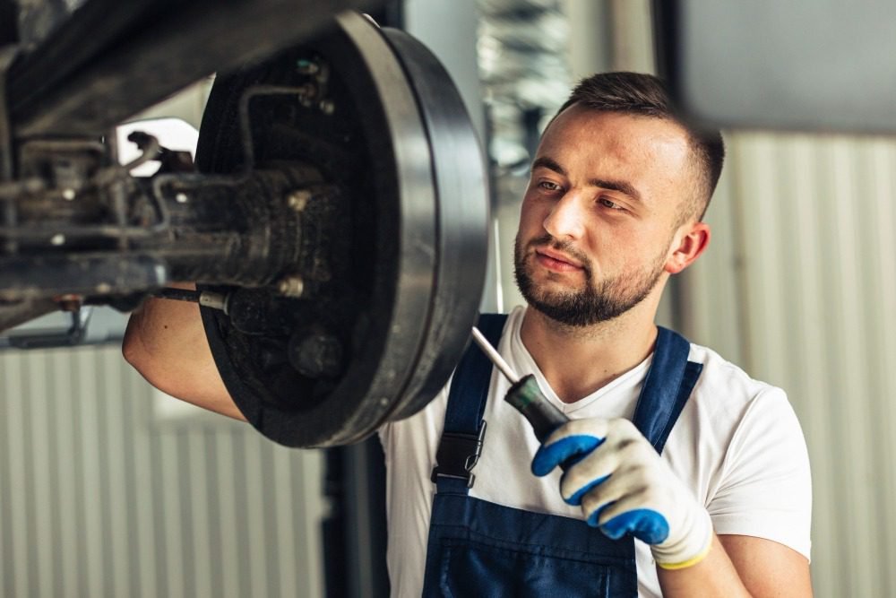 Mechanic in gloves and overalls inspecting and repairing a vehicle Brake Pads system with a screwdriver.