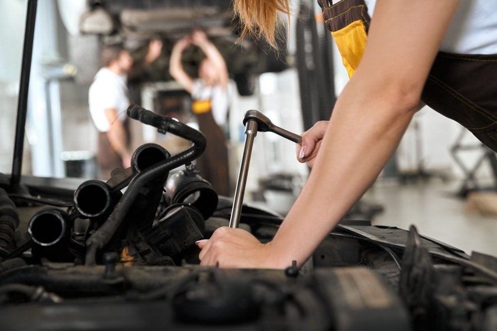 Mechanic using a wrench to repair a car engine in an auto repair shop.