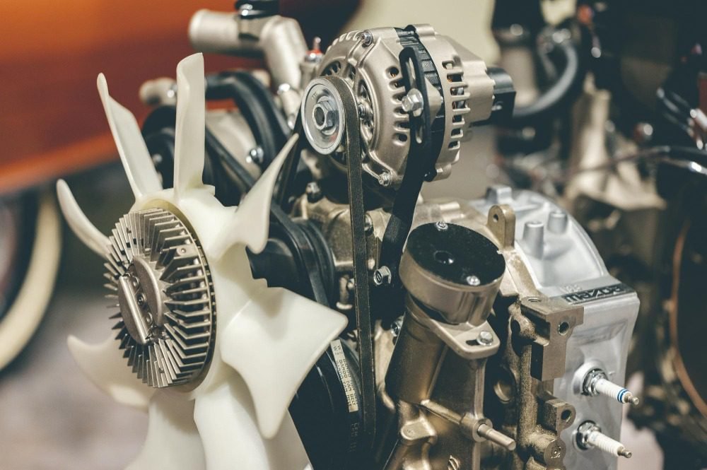 Close-up of car engine showing cooling fan, alternator, drive belt, spark plugs and metal housing.