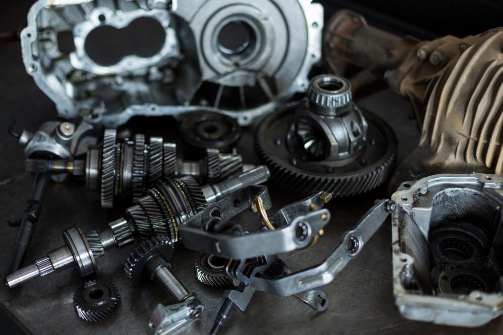 Close-up of disassembled gearbox parts with gears, shafts, and housing placed on a workshop surface.