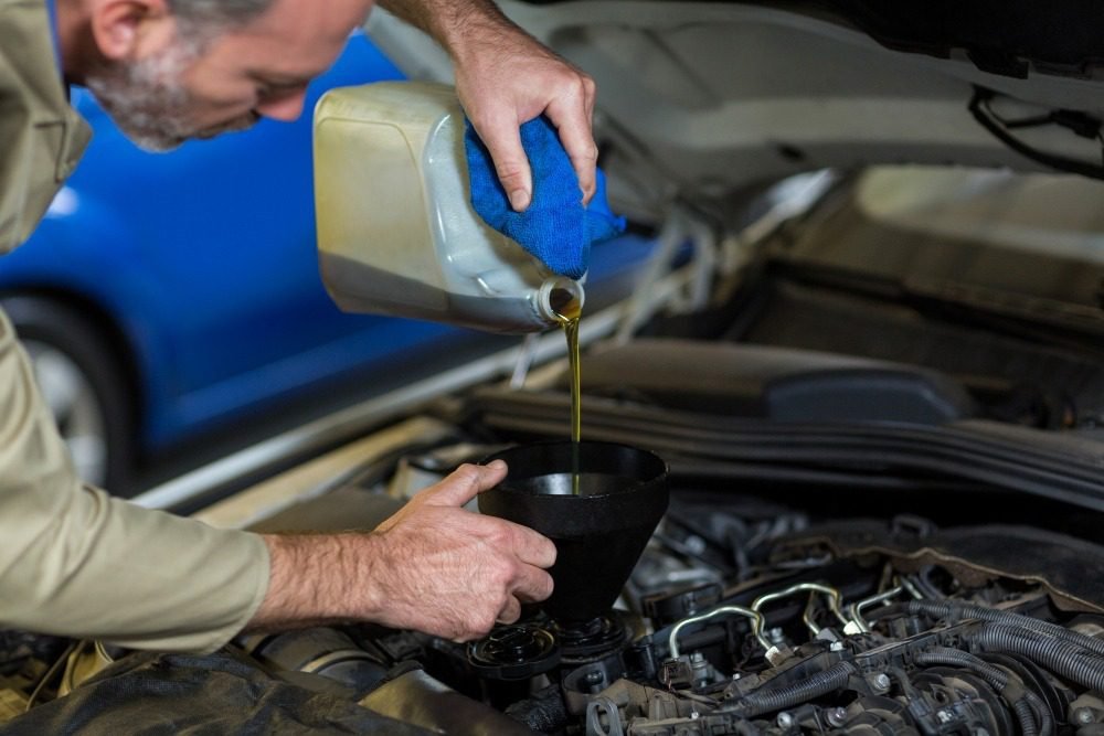 Mechanic pouring engine oil into car using funnel during vehicle maintenance service in workshop.