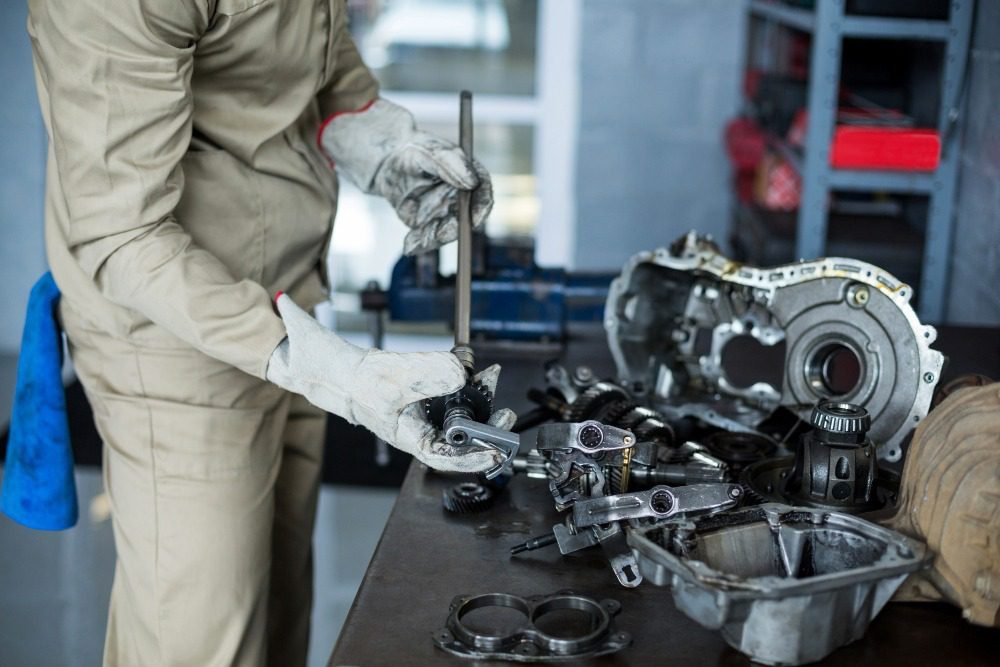 Mechanic wearing gloves assembling gearbox components on workshop table during car repair.