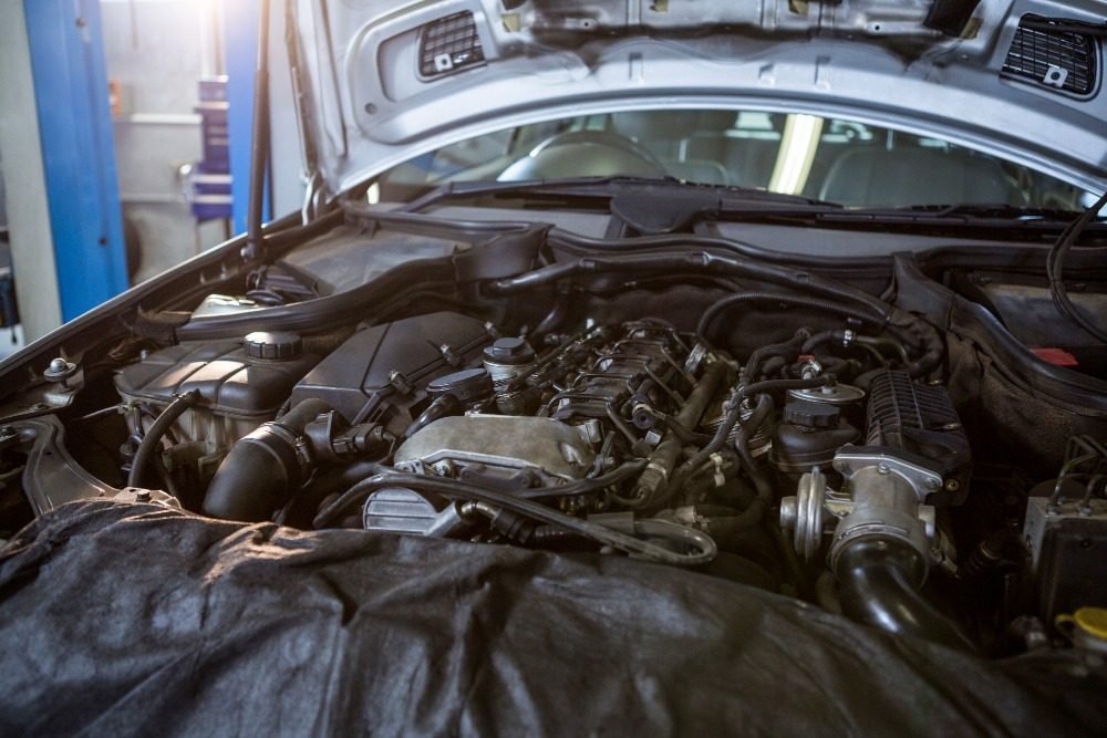 Car engine under the hood with visible components and wiring during repair work in an auto workshop.