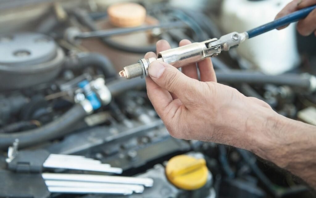 A mechanic's hand holding spark plug with tool during car engine repair and maintenance service.